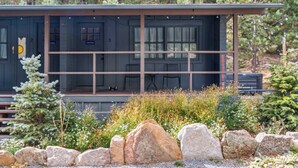 A cabin with a covered porch, a small dining area, and a view of the surrounding forest. - Chief's Head Peak (Allenspark)