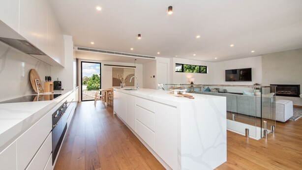 A modern kitchen with a large island, a dining area with a glass partition, and a living space with a sofa and TV. - Pet Friendly - Sandringham Sunshine Escape (Sandringham)