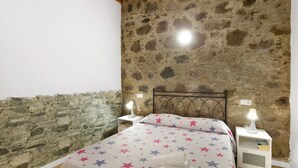 Un dormitorio con pared de piedra, una cama con ropa de cama estampada con motivos de estrellas, dos mesitas de noche con lámparas y techo de madera.