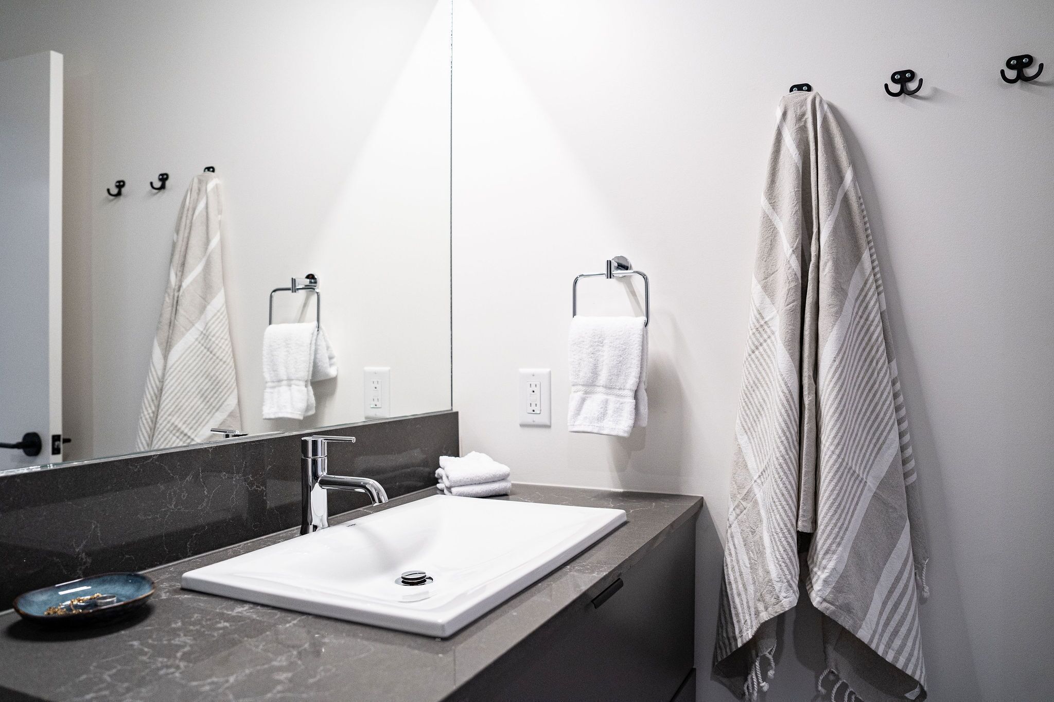 A modern bathroom with a white sink, a large mirror, and towels hanging on hooks.