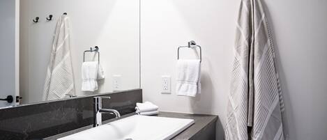 A modern bathroom with a white sink, a large mirror, and towels hanging on hooks.
