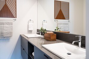 Une salle de bain moderne avec deux vasques, un miroir et un support à plantes en bois.
