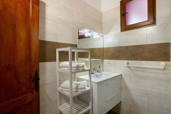 A bathroom with a wooden door, a white vanity with a mirror, and a towel rack.