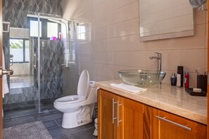 A modern bathroom with a glass shower enclosure, a white toilet, and a wooden vanity with a glass sink.