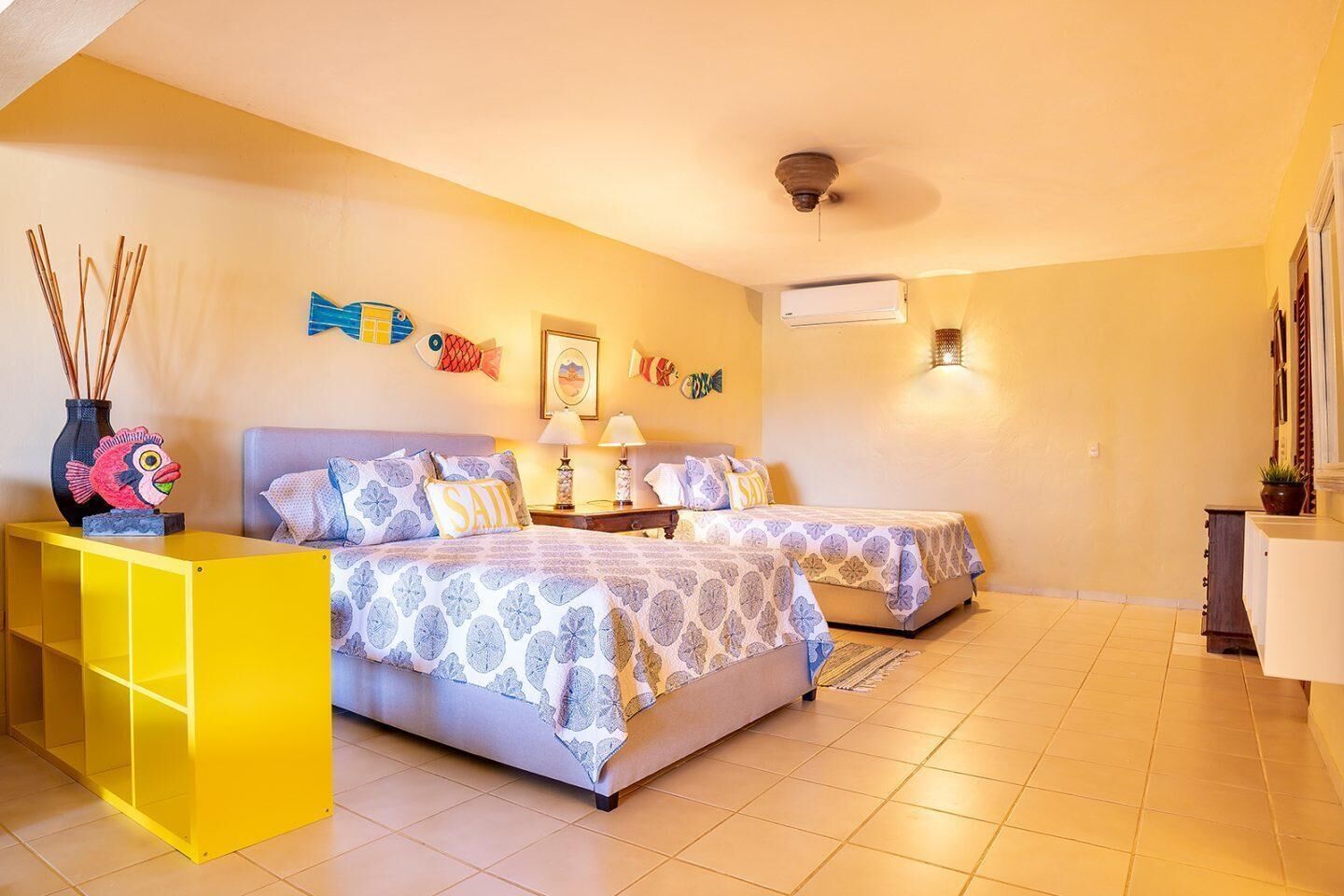 A bedroom with two beds, a yellow side table, a ceiling fan, and wall decorations.