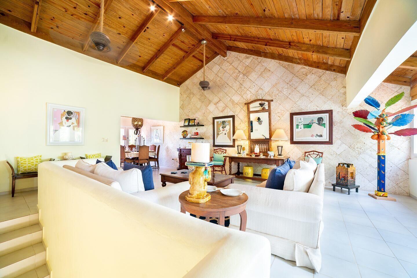A spacious living area with a high wooden ceiling, a dining area, and a kitchen in the background.