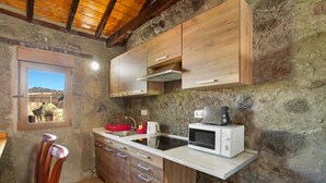 A rustic kitchen with wooden cabinets, a built-in microwave, and a window with a view of the mountains. - Vacation Home 'Villa Paraiso Aldeano 1' with Mountain View, Shared Pool and Wi-Fi (La Aldea de San Nicolás)