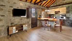 A rustic kitchen with stone walls, wooden beams, a TV, a wooden cabinet, and a dining area with chairs. - Vacation Home 'Villa Paraiso Aldeano 1' with Mountain View, Shared Pool and Wi-Fi (La Aldea de San Nicolás)