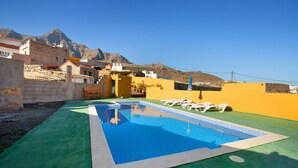 A swimming pool with a clear blue water, surrounded by a green surface, and white lounge chairs. - Vacation Home 'Villa Paraiso Aldeano 1' with Mountain View, Shared Pool and Wi-Fi (La Aldea de San Nicolás)