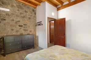 A bedroom with a bed, a dresser, a wooden door, and a stone wall.