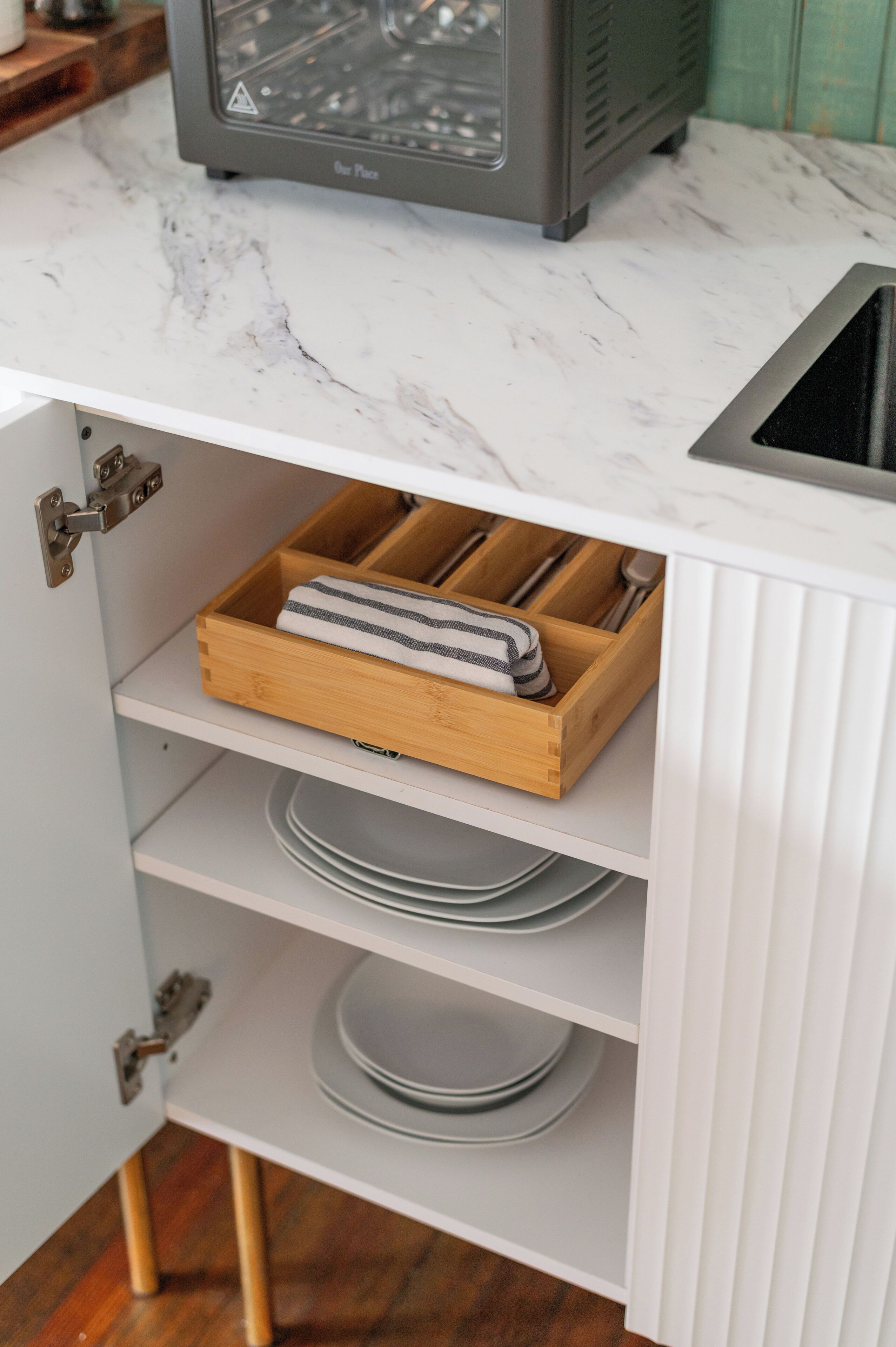 Una cocina con encimera de mármol, horno empotrado y organizador de cajones con utensilios.