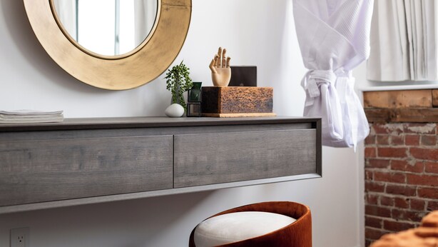 A modern bathroom with a round mirror, a wooden vanity, a towel rack, and a brick wall. - Blueprint Suite at Spofford Lodge (Bucksport)