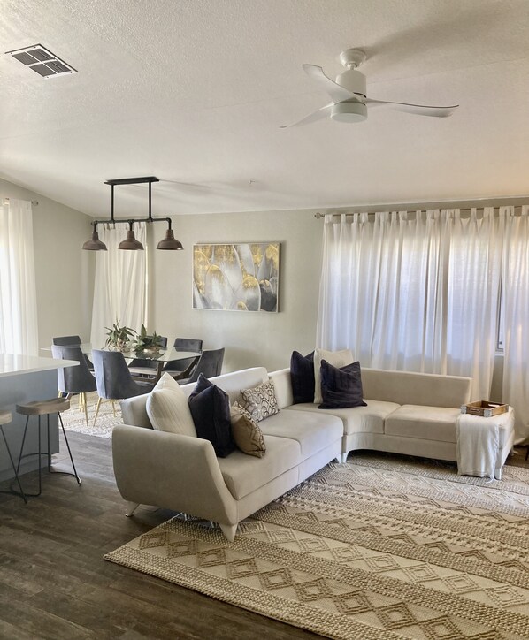 A modern living room with a white sofa, a dining area with a table and chairs, and a ceiling fan.