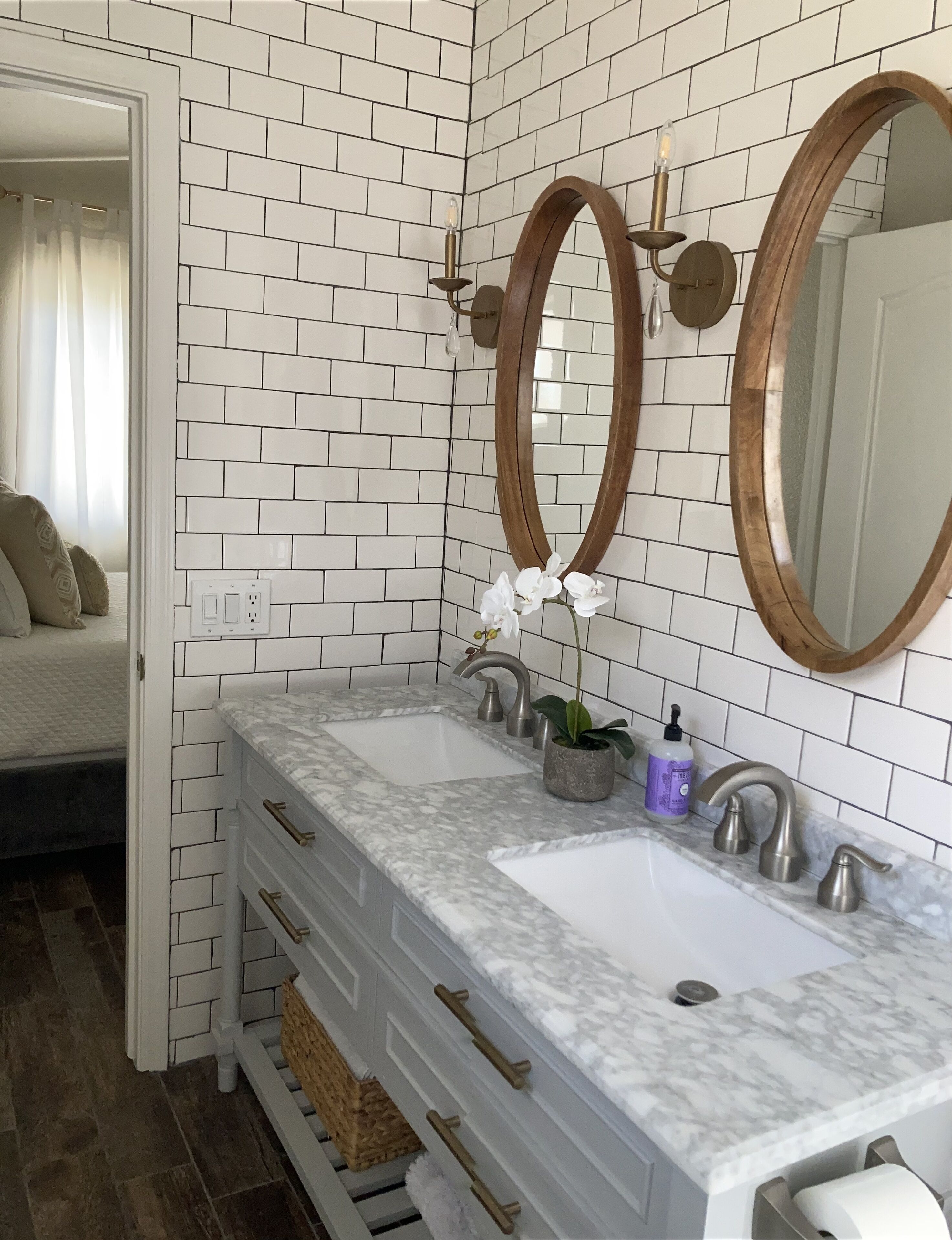 A bathroom with white brick walls, two sinks with marble countertops, a wooden-framed mirror, and a potted orchid.