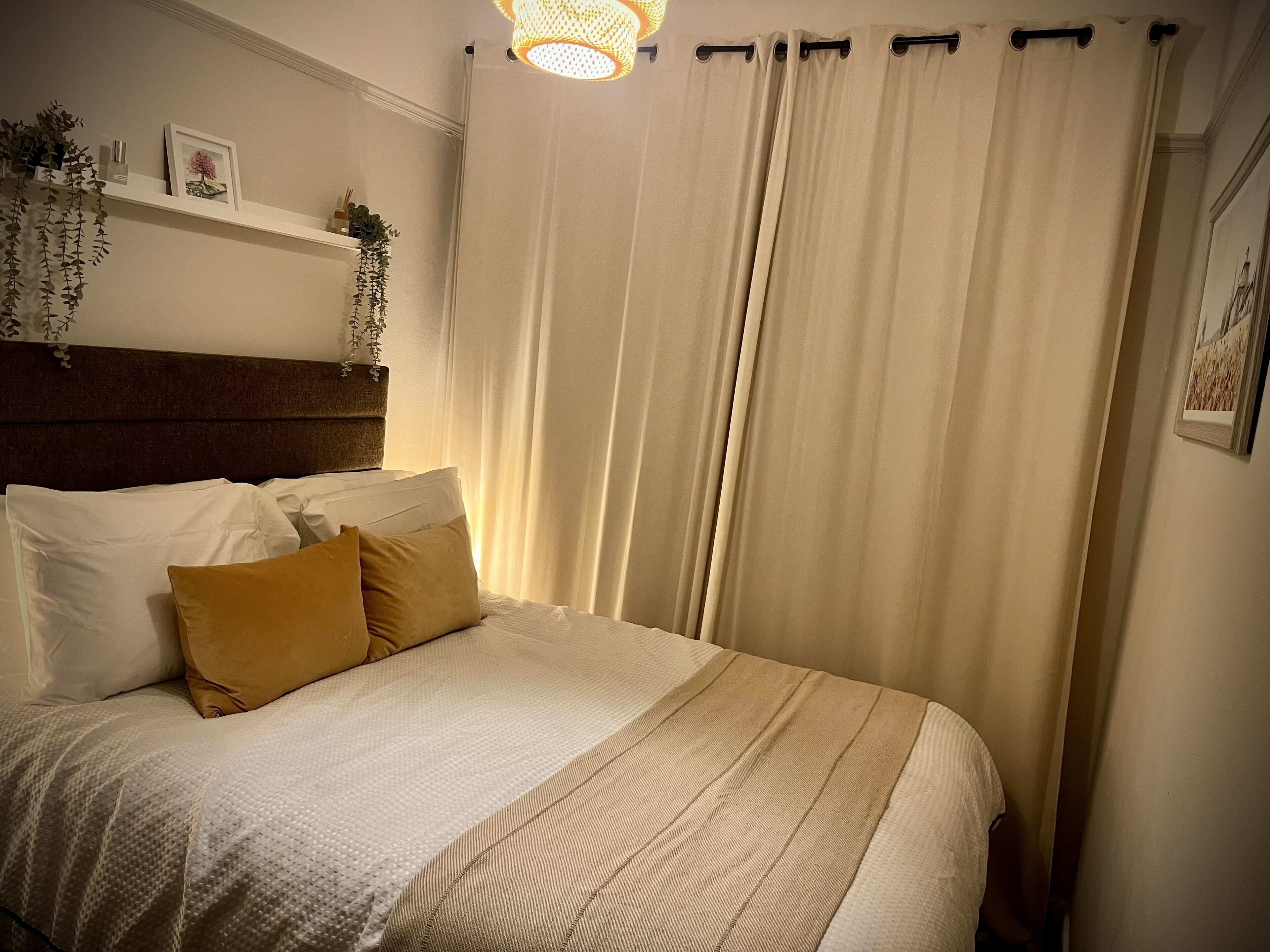 Een net opgemaakt bed met witte en mosterdkleurige kussens, een hoofdbord en een hangplant.