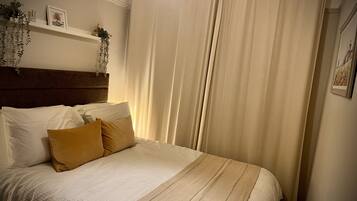 Een net opgemaakt bed met witte en mosterdkleurige kussens, een hoofdbord en een hangplant.