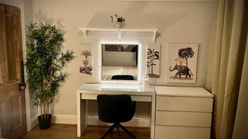 A bedroom with a white desk, a black chair, a large mirror, and a potted plant.