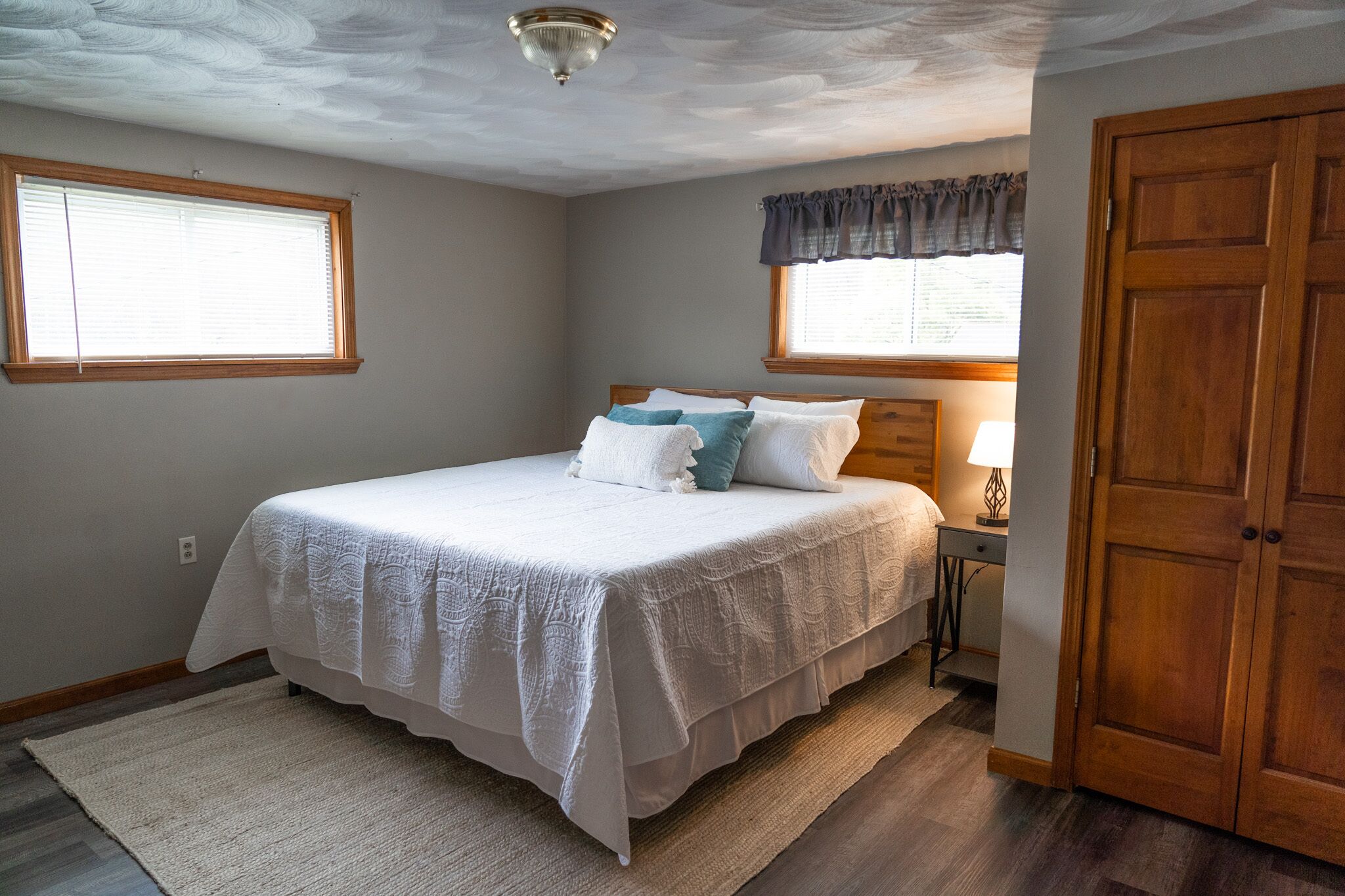 Une chambre à coucher avec un grand lit, une table de chevet, une lampe, une armoire en bois et une fenêtre avec des stores.
