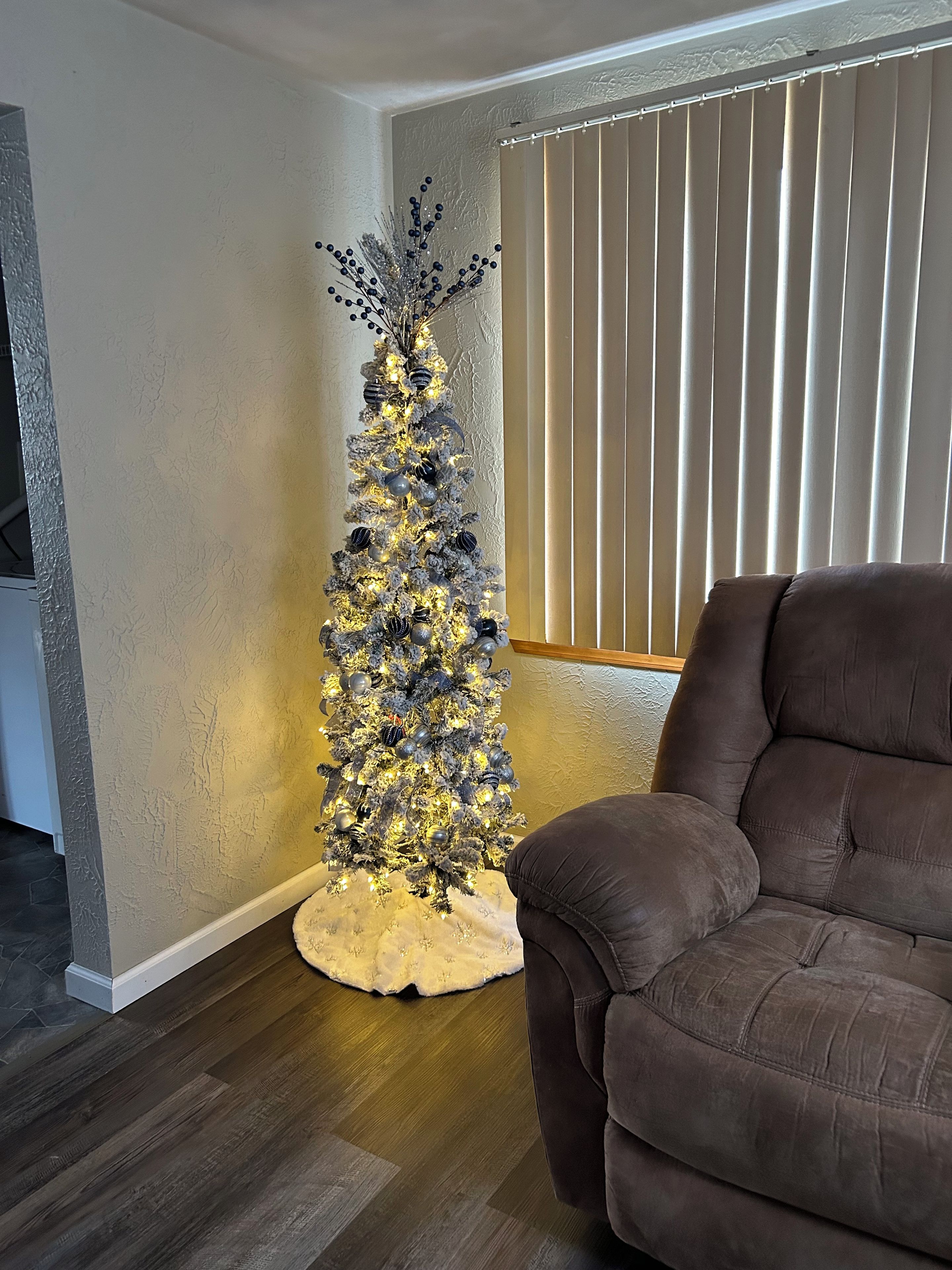 Un salon avec un canapé en cuir marron foncé, un mur blanc à texture et un sapin de Noël illuminé.