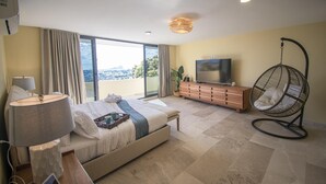 Ett modernt hotellrum med en stor säng, en TV, en hängstol och utsikt över staden.