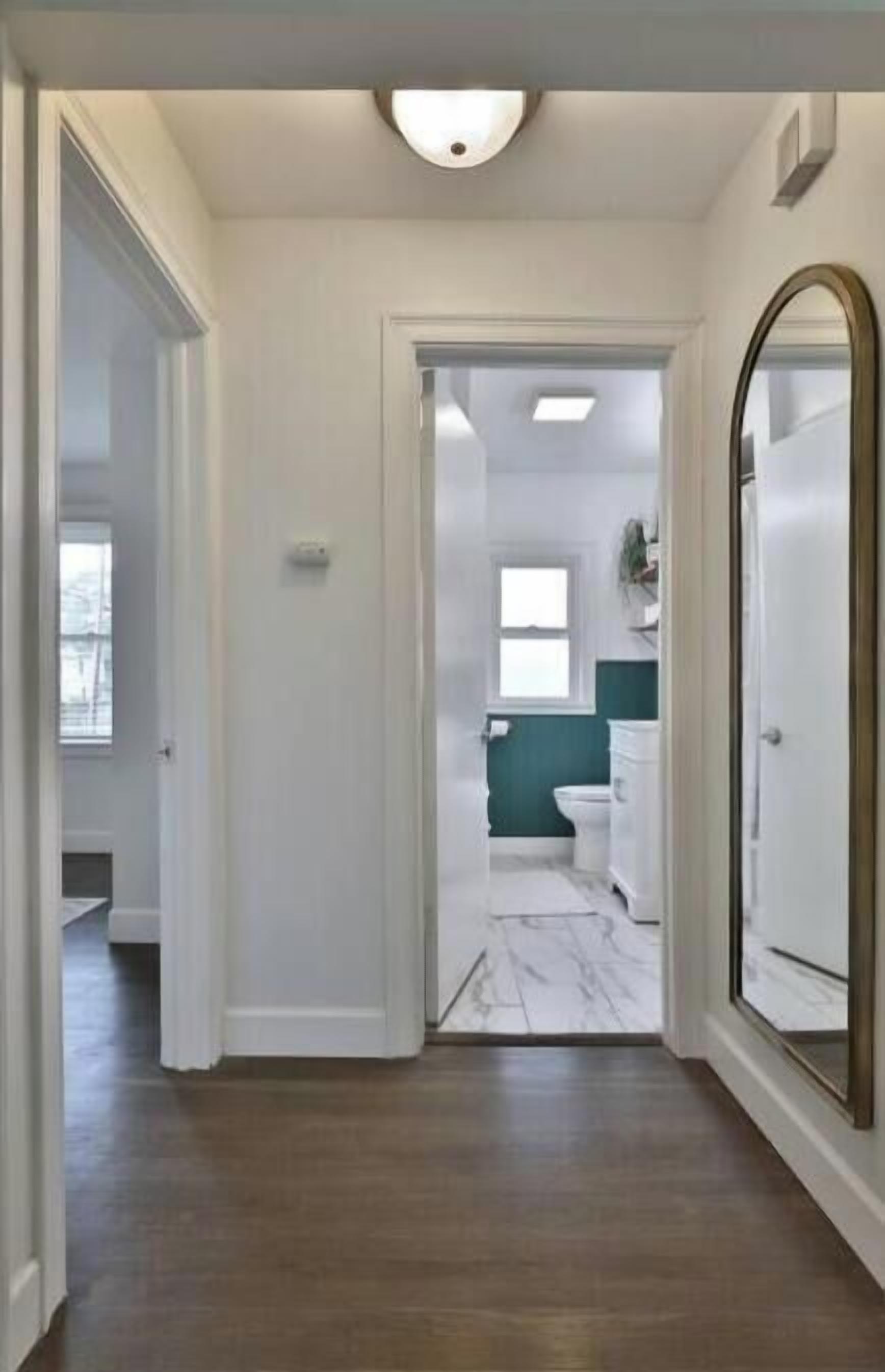 A hallway leading to a bathroom with a marble floor, white walls, and a green accent wall.