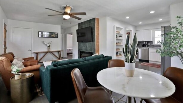 A modern living room with a green sofa, a brown leather chair, a white marble table, and a ceiling fan. - Clintonville Cottage- Close to OSU & Downtown (Columbus)