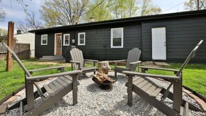A black house with a fire pit in the center, surrounded by Adirondack chairs. - Clintonville Cottage- Close to OSU & Downtown (Columbus)