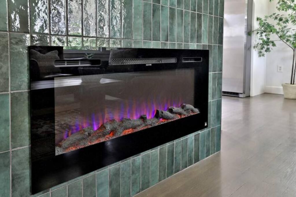 Een moderne woonkamer met een grote flatscreen televisie aan de muur, een open haard met daarin een vlam, en een potplant in de hoek.