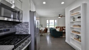 A modern kitchen with stainless steel appliances, a dining area with a green sofa, and a white shelving unit. - Clintonville Cottage- Close to OSU & Downtown (Columbus)