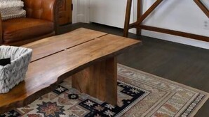 A room with a wooden door, a brown leather sofa, a wooden coffee table, a patterned rug, and a small table with a vase and flowers. - Clintonville Cottage- Close to OSU & Downtown (Columbus)