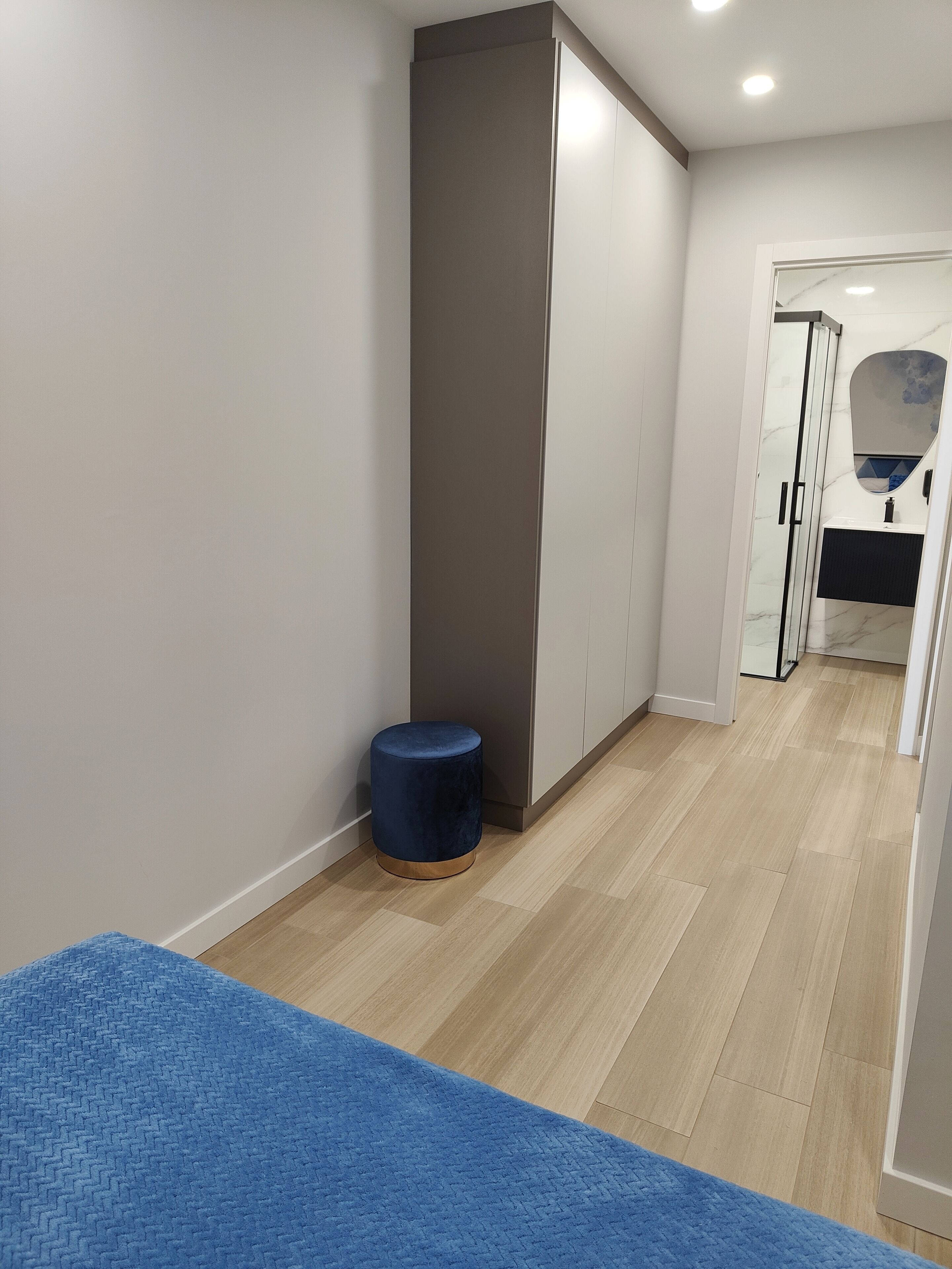 Una habitación de hotel moderna con un armario grande, un taburete redondo pequeño y una alfombra azul en el suelo.