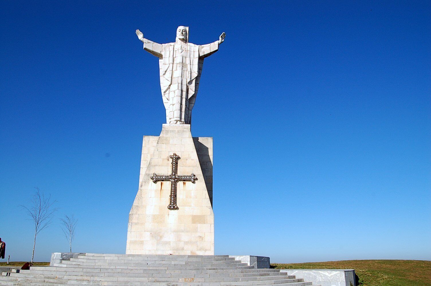A large statue with outstretched arms on a pedestal with a cross.