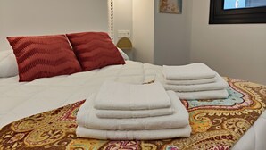 A neatly made bed with white linens and red pillows, a patterned rug, and a window with a view. - Elegancia y Modernidad en el Punto más Céntrico de Oviedo (Oviedo)