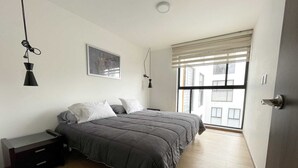 A bedroom with a bed, bedside tables, a window with blinds, and a painting on the wall.