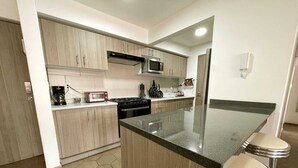 A modern kitchen with light wood cabinets, a central island with bar stools, a microwave, stove, and a refrigerator.