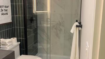 A bathroom with a glass-enclosed shower, a toilet, a sink, and a towel rack.