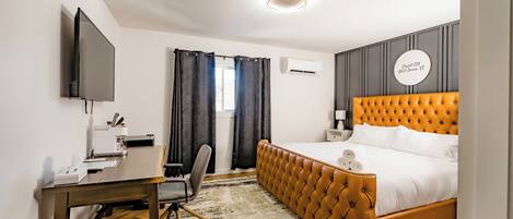 Una habitación de hotel moderna con una cama grande, un escritorio con silla, un televisor de pantalla plana y un equipo de aire acondicionado.