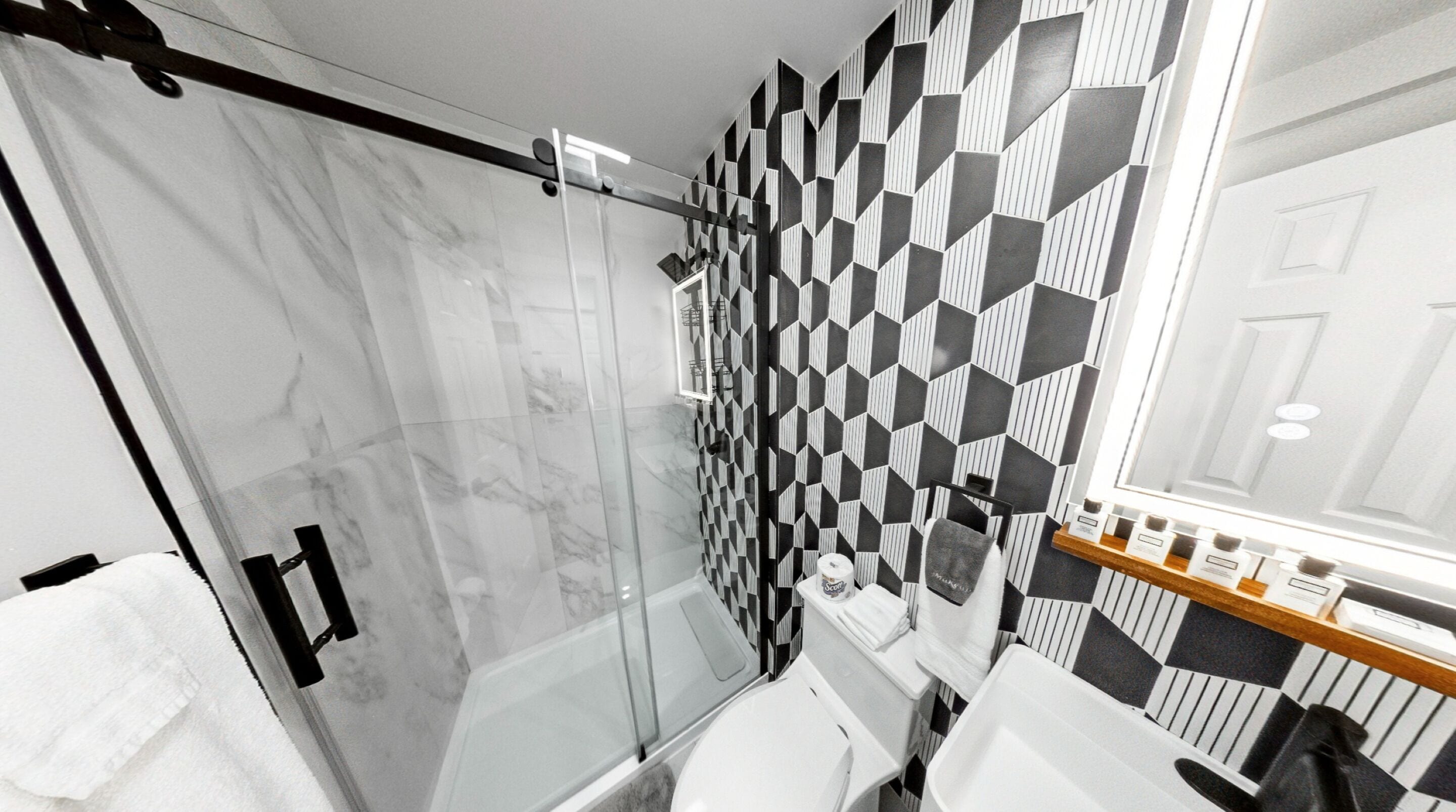 Ein modernes Badezimmer mit Duschkabine aus Glas, Wand mit geometrischem Muster und Holzwaschtisch mit Spiegel.