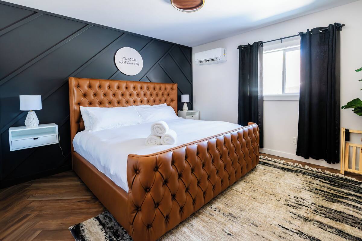 A modern bedroom with a tufted brown headboard, white bedding, and a circular sign on the wall.