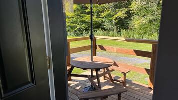 Relax on the deck surrounded by lush greenery, with a round table and bench for a peaceful retreat.