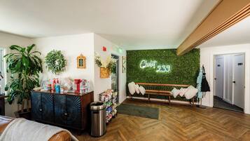 A lobby with a wooden herringbone floor, a bench with cushions, a neon sign reading "Chalet 239", and a green wall with foliage.