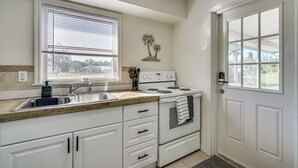 Una cocina con gabinetes blancos, estufa, lavabo y una ventana con persianas.