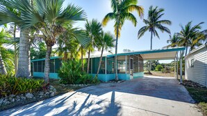 Una casa moderna con un porche cubierto, rodeada de palmeras y plantas tropicales.