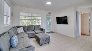 Una sala de estar con sofá seccional, reposapiés y televisor de pantalla plana montado en la pared.