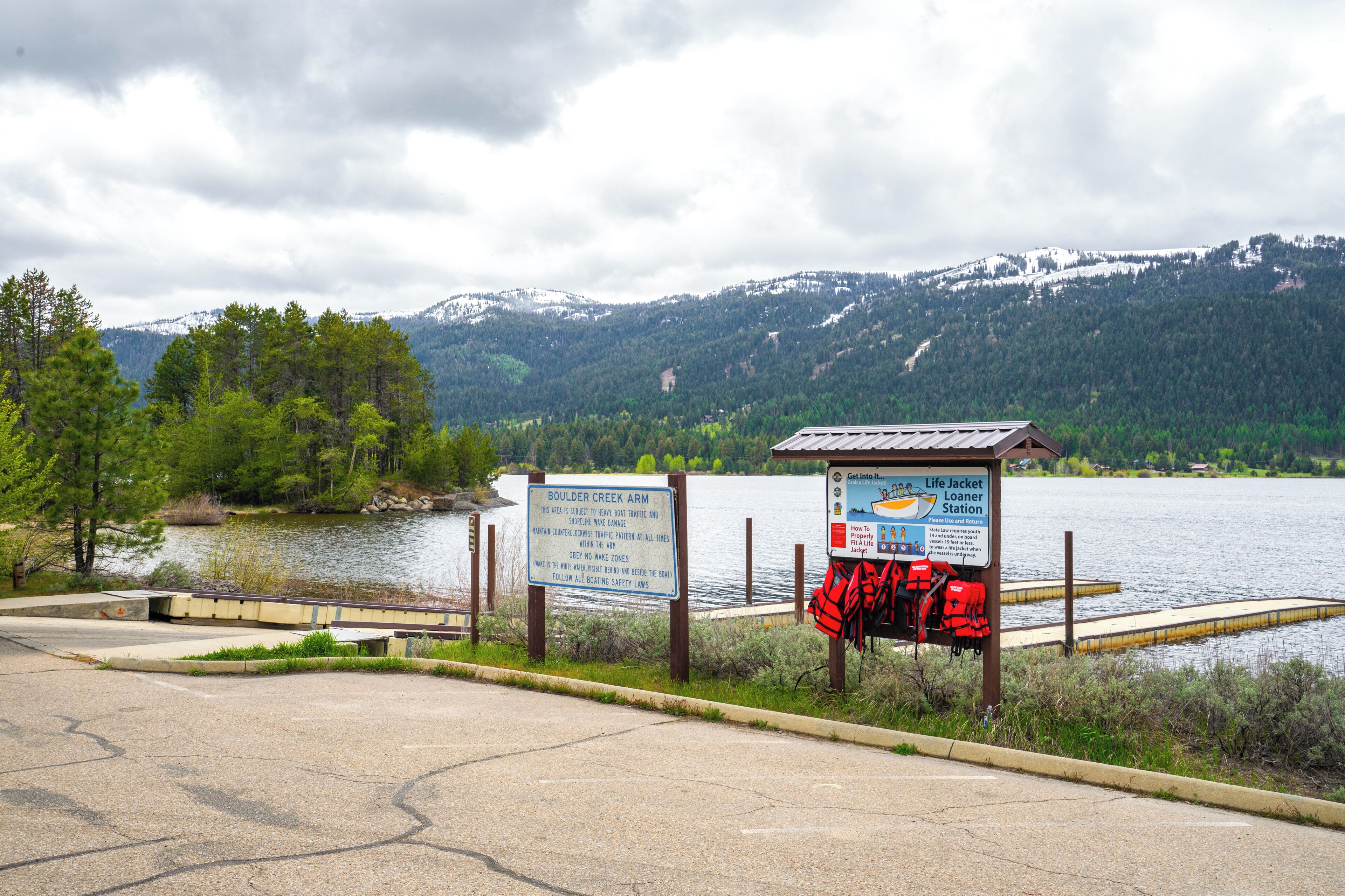 A lakeside parking area with a life jacket station and informational signs.
