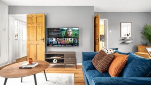 A living room with a TV mounted on the wall, a blue sofa, a wooden coffee table, and a wooden door.