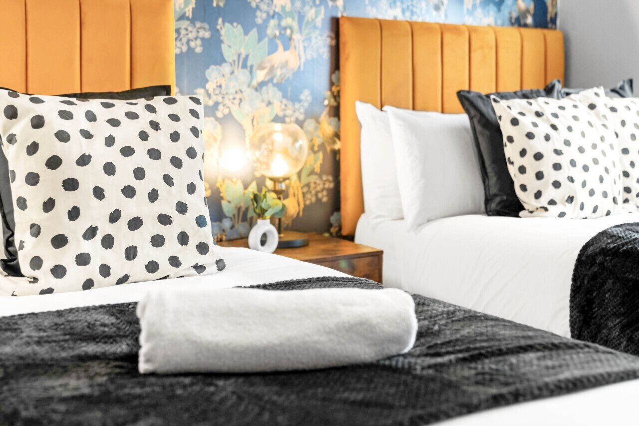 Habitación de hotel con cama, almohadas, mesita de noche y lámpara.