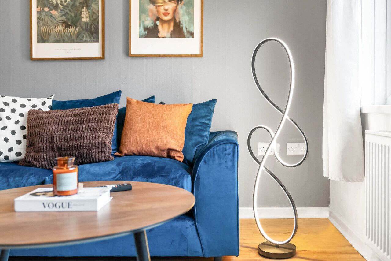 Ein modernes Wohnzimmer mit einem blauen Sofa, einem runden Couchtisch aus Holz und zwei gerahmten Pflanzenbildern an der Wand.