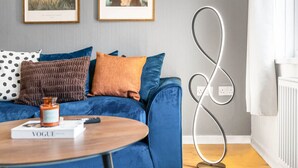 A modern living room with a blue sofa, a round wooden coffee table, and two framed botanical prints on the wall.
