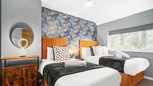 A hotel room with two beds, a round mirror, a wooden cabinet, and a window with a view.